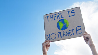 Two hands holding a sign up in the air, with a drawing of the Earth and the words "There is no planet B".