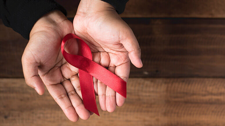 Two hands cupped together, palms open, holding a red Aids ribbon.